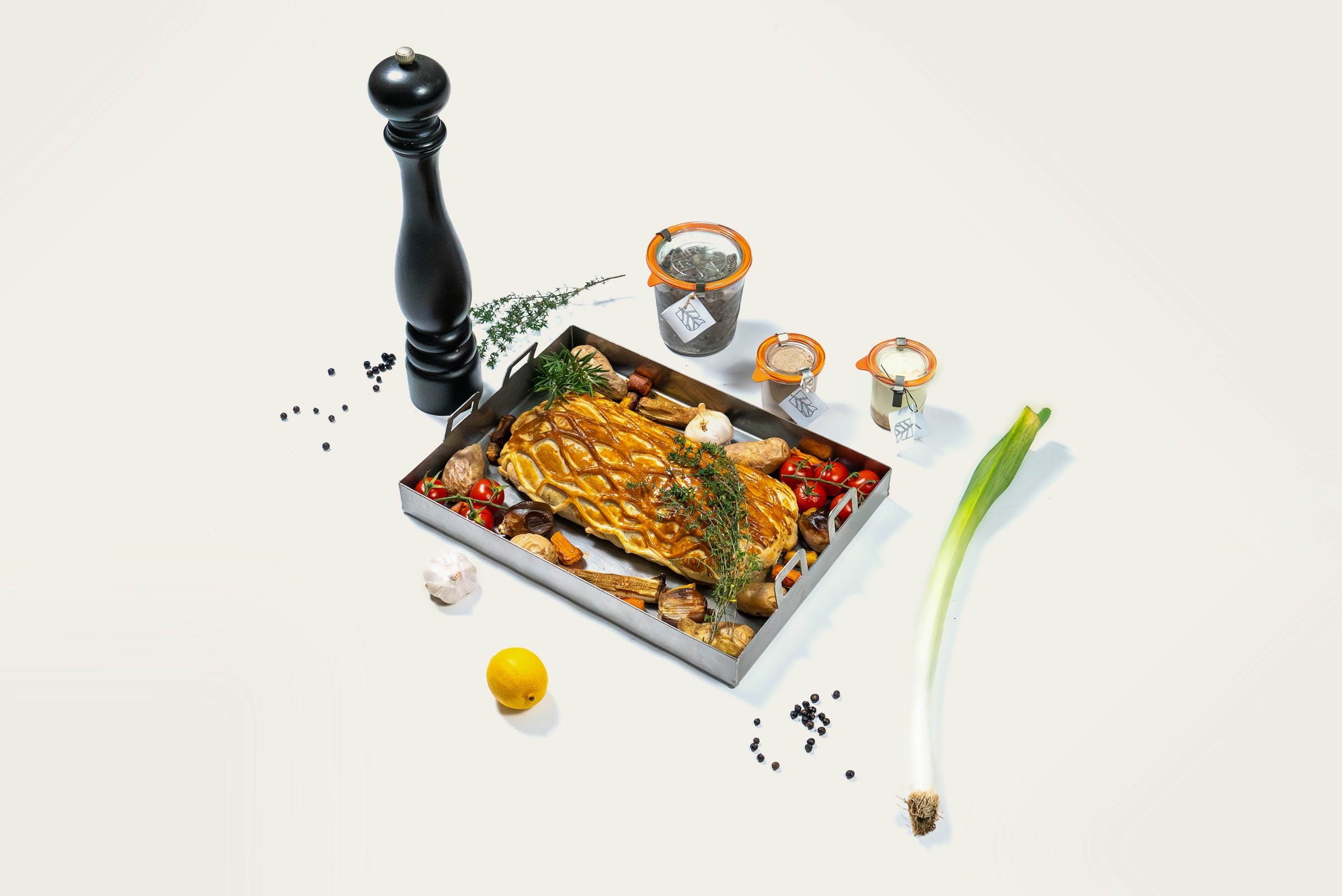 Knusprig gebratenes Schweinefleisch in einer Metallkiste mit Kartoffeln, Paprika, Knoblauch und frischen Kräutern wie Rosmarin, umgeben von Gewürzen und Lauchzwiebel – appetitliche Foodaufnahme zum Thema kistenfleisch selber machen für Grill oder Ofen.